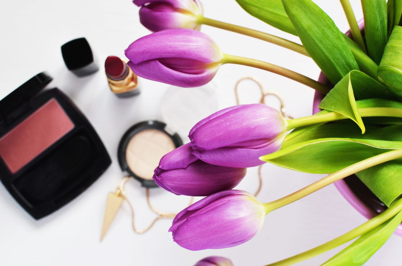Purple tulips and makeup create a stylish beauty flat lay.