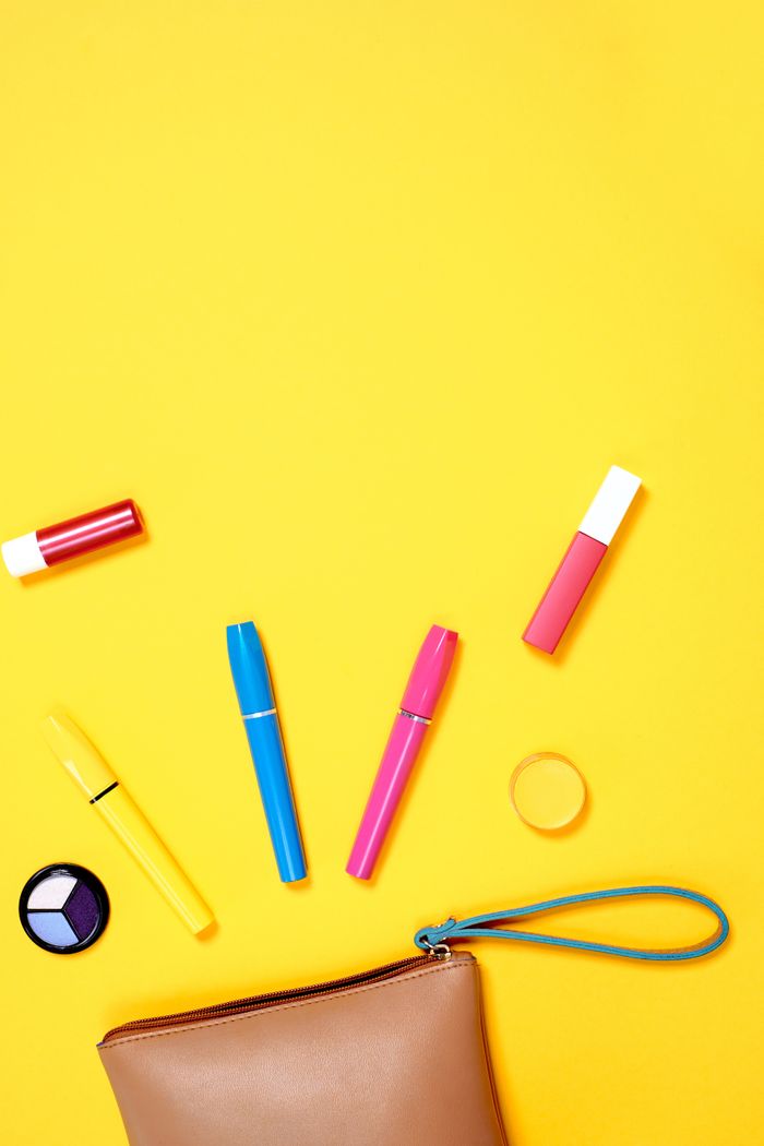 Flatlay of assorted colorful cosmetics with ample copy space on a bright yellow background.