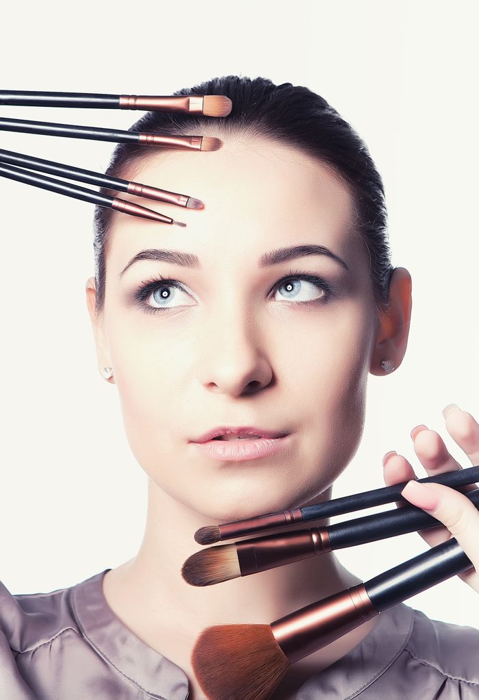 Portrait of a woman surrounded by makeup brushes, highlighting beauty techniques.